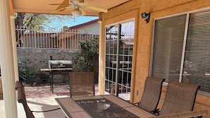 Eine Terrasse im Freien mit Tisch, Stühlen, Deckenventilator und Grill.