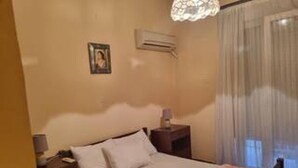 A bedroom with a bed, a nightstand, a lamp, a picture on the wall, and an air conditioning unit. - Lovely 1-bed Apartment in Athina (Athens)