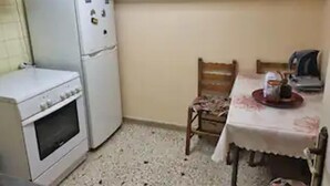 A small kitchen with white cabinets, a refrigerator, an oven, and a dining table with chairs. - Lovely 1-bed Apartment in Athina (Athens)