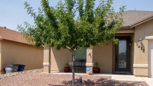 A residential house with a tree in the front yard, a door with a number, and a trash bin.