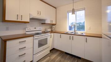 A modern kitchen with white cabinets, a stainless steel sink, and a window providing a view of the city.