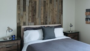 A bedroom with a wooden headboard, a bed with white and gray bedding, two bedside tables with lamps, and a ceiling fan.