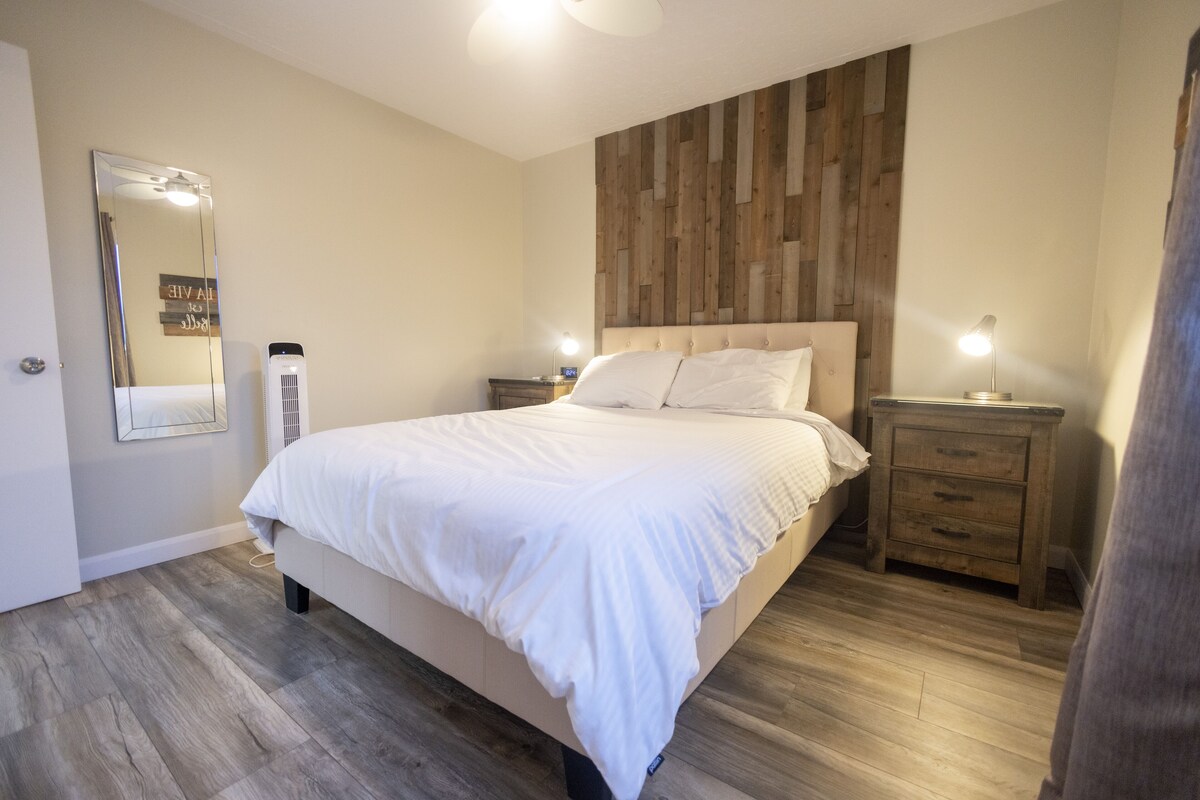 A bedroom with a large bed, wooden headboard, bedside tables with lamps, and a mirror on the wall.