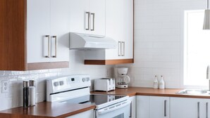 A modern kitchen with white cabinets, a built-in oven, a stove, a coffee maker, and a sink.