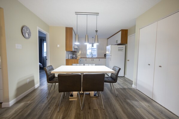 A modern kitchen with a central island, pendant lights, and a dining area with a white table and chairs. - Le Contemporain (Rouyn-Noranda)