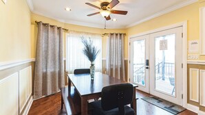 Un comedor con mesa de madera, sillas, ventilador de techo y vista al exterior.