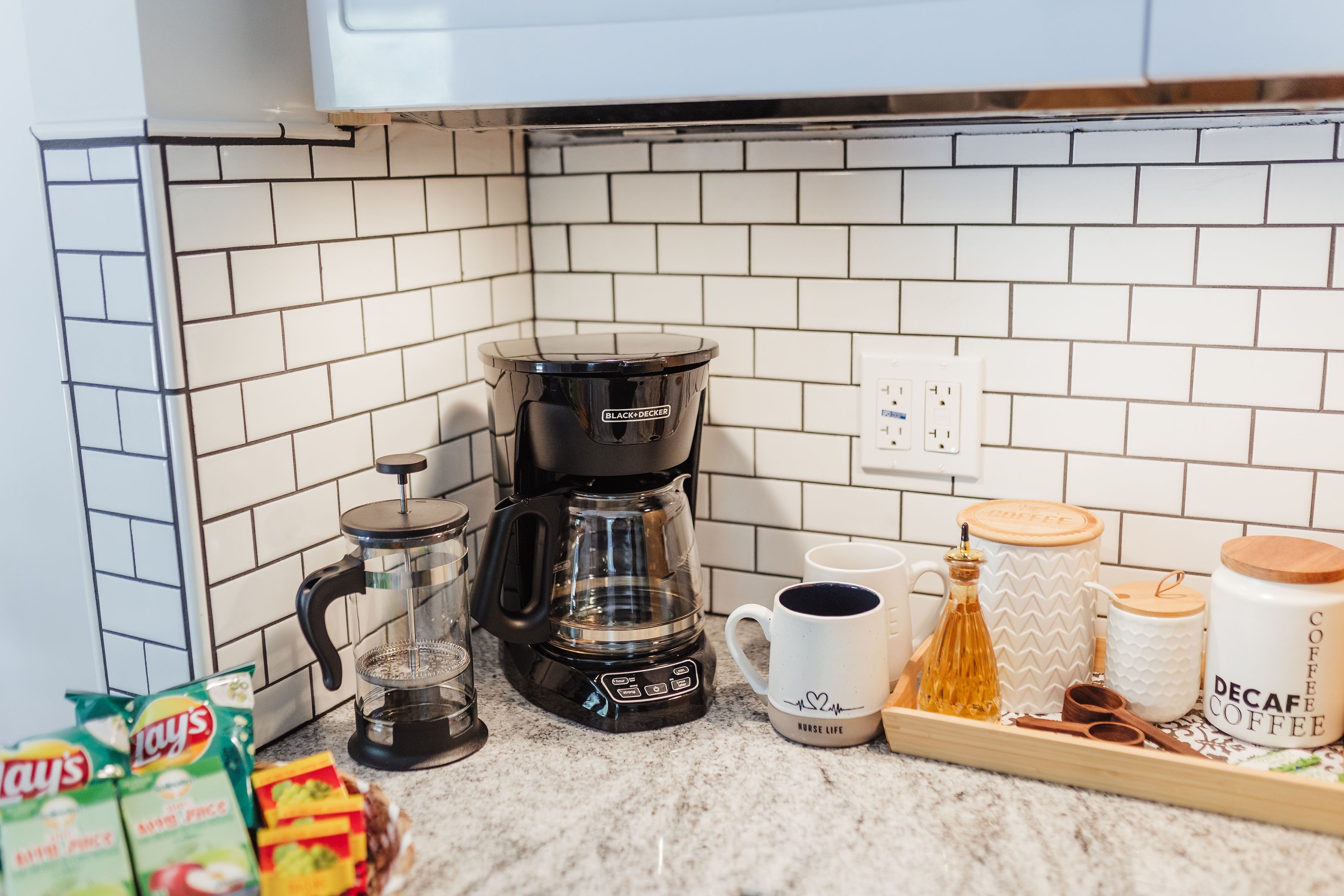 A kitchen with a coffee maker, a glass carafe, a mug, and a tray with coffee containers.
