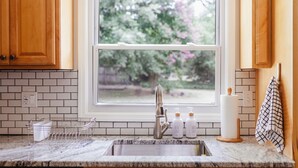Una cocina con ventana, un lavabo, un escurreplatos y dos botellas de jabón.