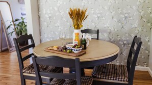 Una mesa redonda de comedor con un jarrón de espigas secas, un vaso de zumo de naranja y una botella de aceite de oliva.