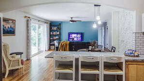 Un comedor con una mesa de mármol, sillas blancas, un ventilador de techo y un televisor en la pared.