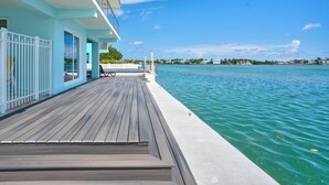Une terrasse en bois avec un espace aménagé au bord de la piscine, une balustrade blanche et une vue sur l’océan.