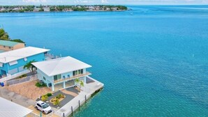 Une propriété située au bord de l’eau, avec une grande maison dotée d’un balcon, d’une allée et d’une voiture garée.