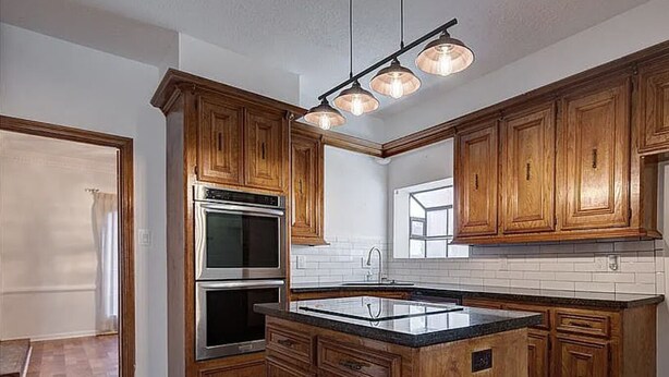 Una cocina con gabinetes de madera, una isla central, electrodomésticos de acero inoxidable e iluminación colgante.