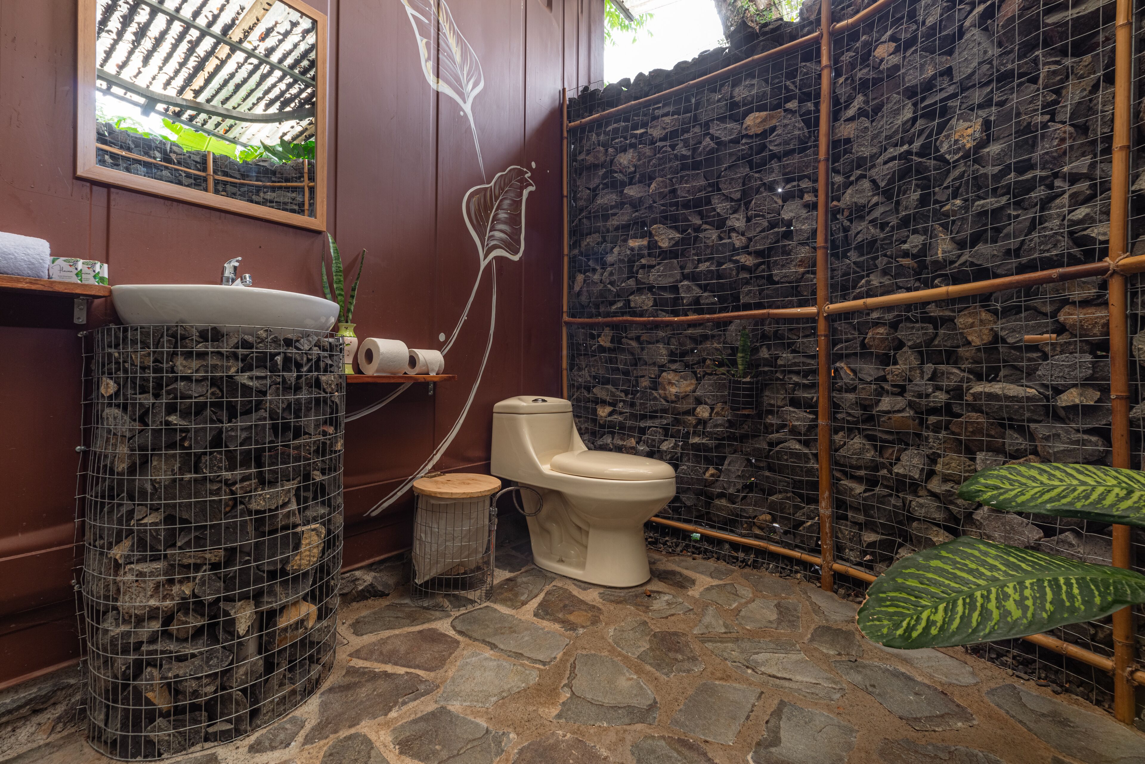 A bathroom with a stone floor, a white sink, a toilet, and a mirror.