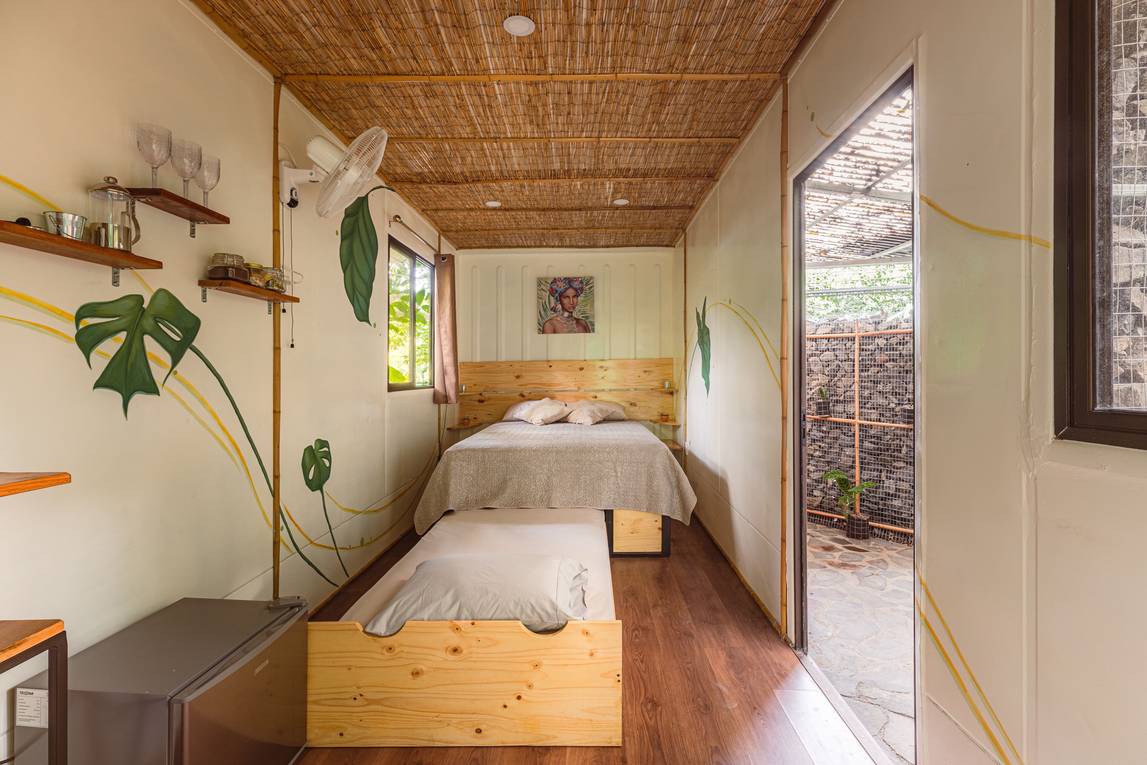 A bedroom with a wooden ceiling, two beds, a desk, and a window.