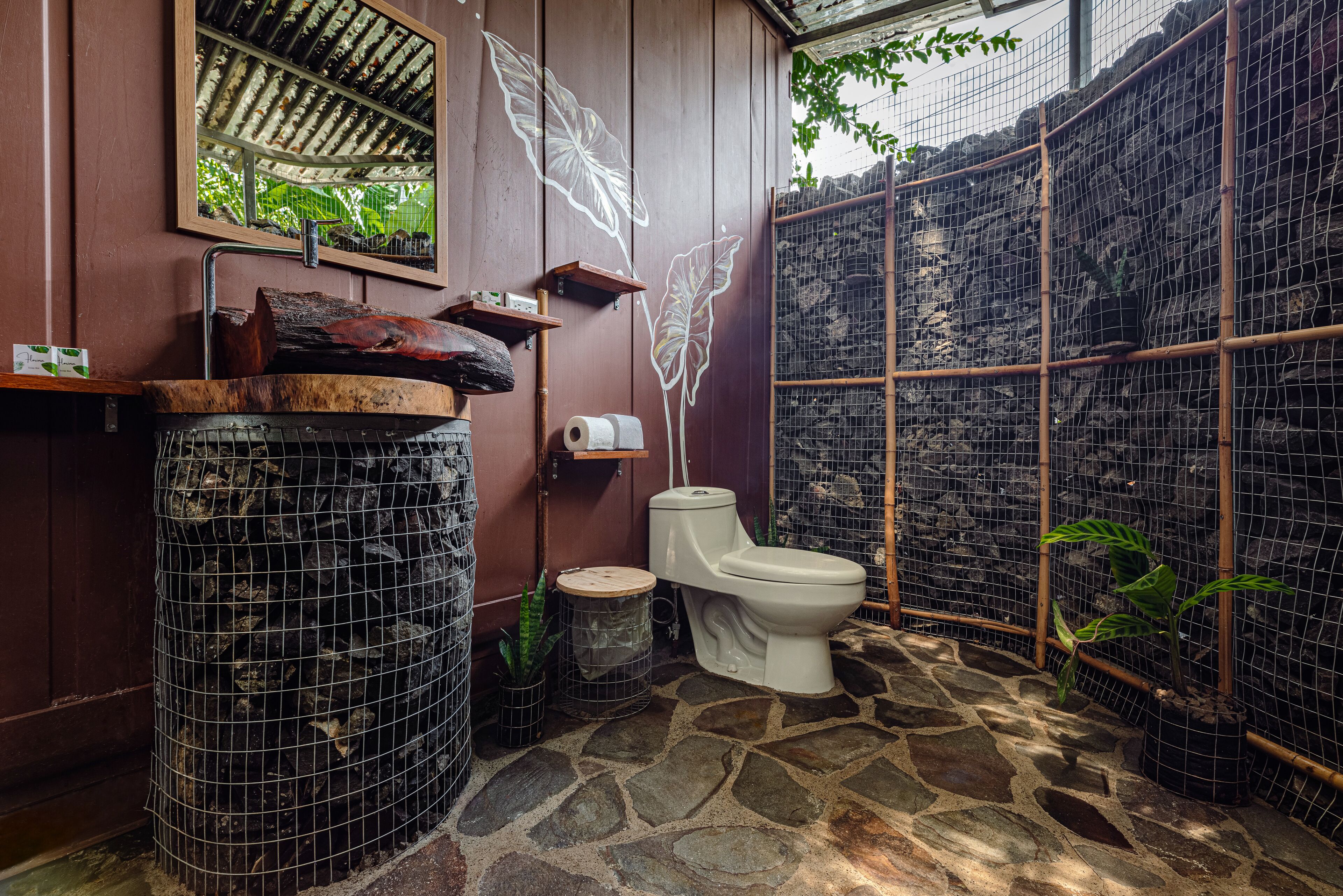 A bathroom with a stone floor, a toilet, a sink with a wooden countertop, and a mirror.