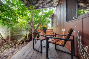 Pátio externo com mesa e cadeiras de madeira, rodeado por vegetação e um muro de concreto.