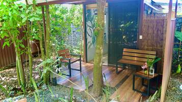 A wooden deck with a bench and a small table, surrounded by greenery and a bamboo fence.