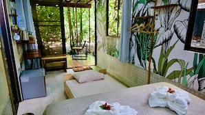 A room with two beds, a small table, a chair, a window with a view of greenery, and a wall with a plant mural. - Terminal Verde (Concepcion)