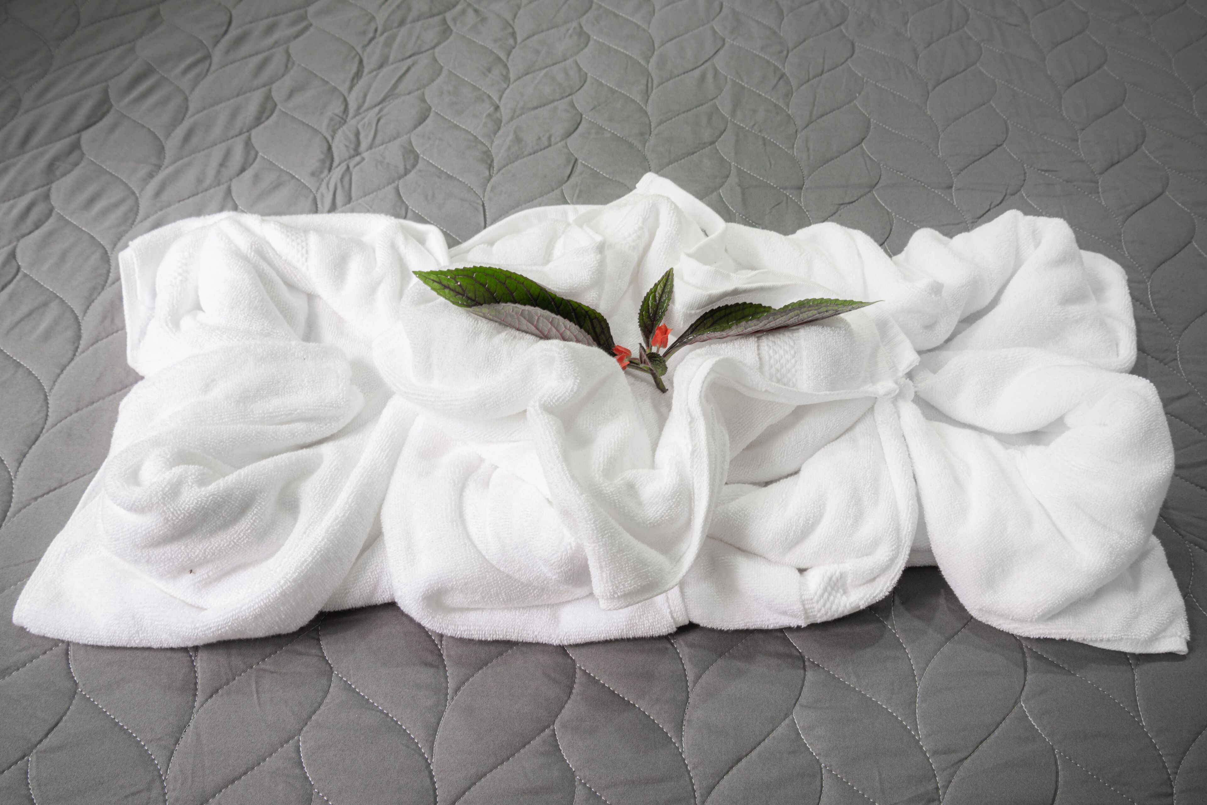 Una tovallola blanca i arrugada amb un petit flore ornamental sobre un estovat gris acolxat.
