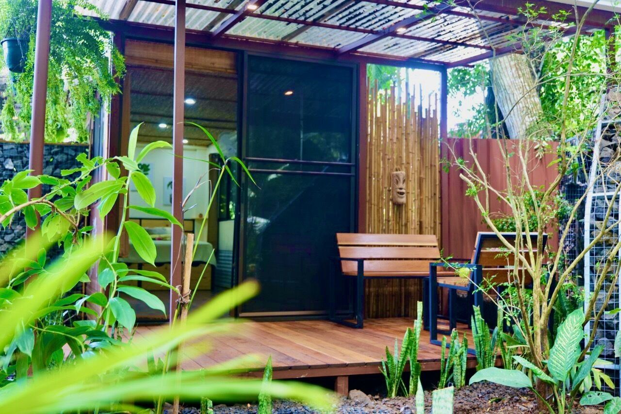 A covered outdoor seating area with a wooden bench and a glass door leading to a room.