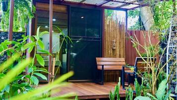 A covered outdoor seating area with a wooden bench and a glass door leading to a room.