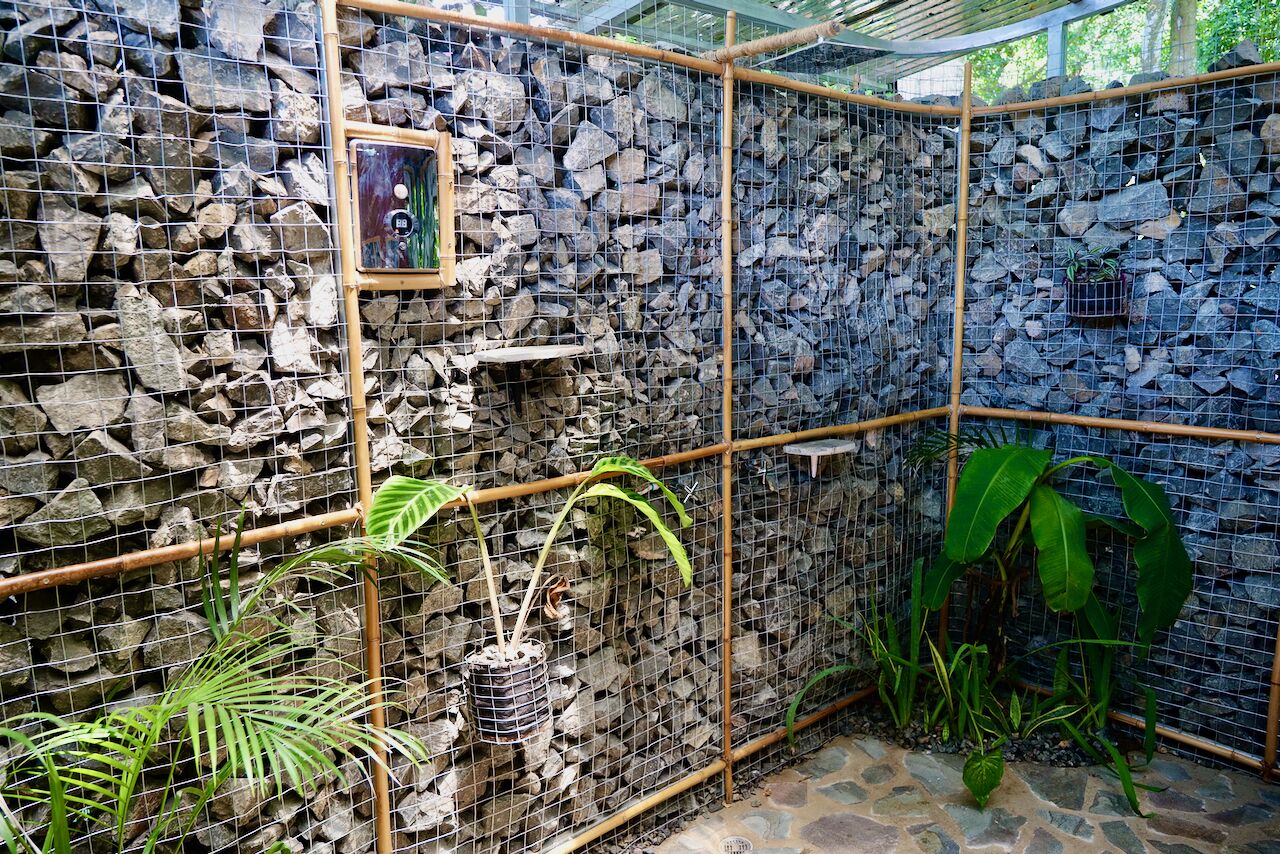 A stone-walled enclosure with a bamboo frame, potted plants, and a framed picture on the wall.