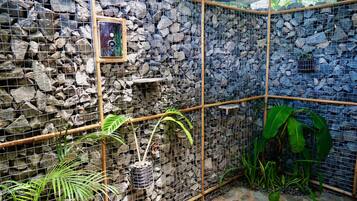 A stone-walled enclosure with a bamboo frame, potted plants, and a framed picture on the wall.