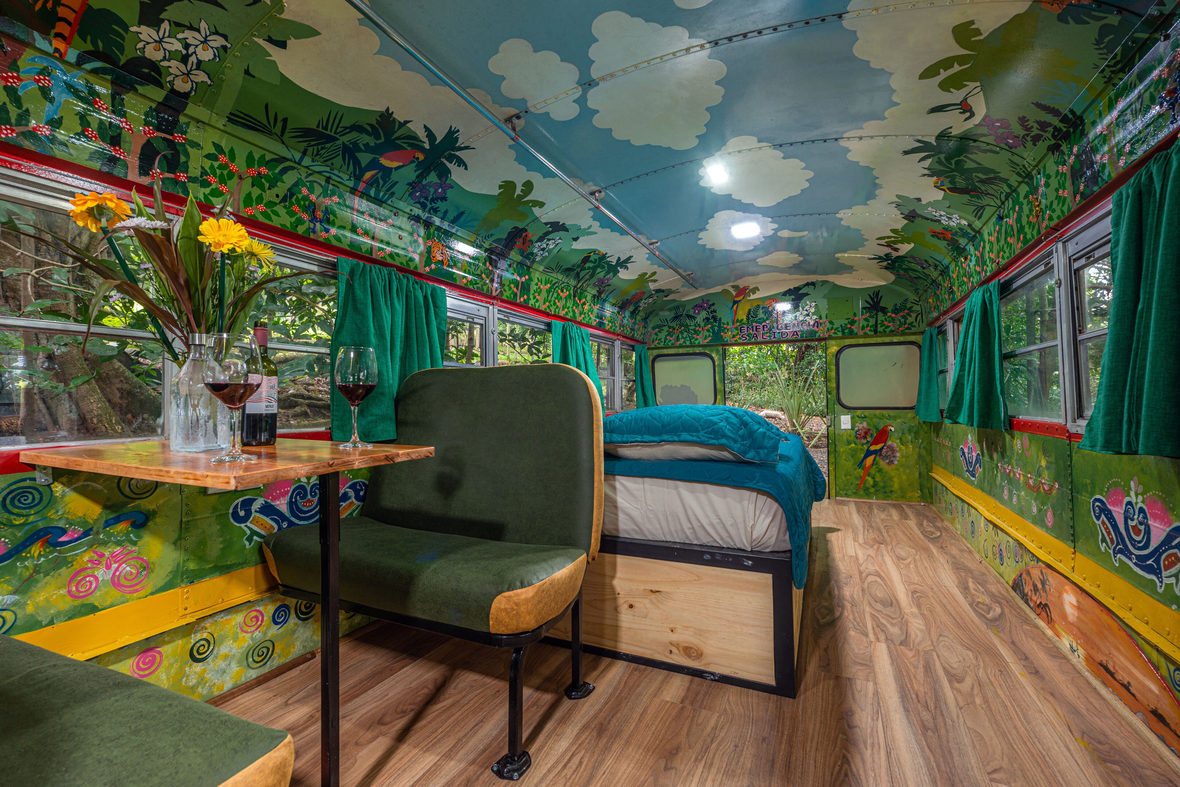 A room with a bed, a chair, a table with a vase of flowers, and a window.