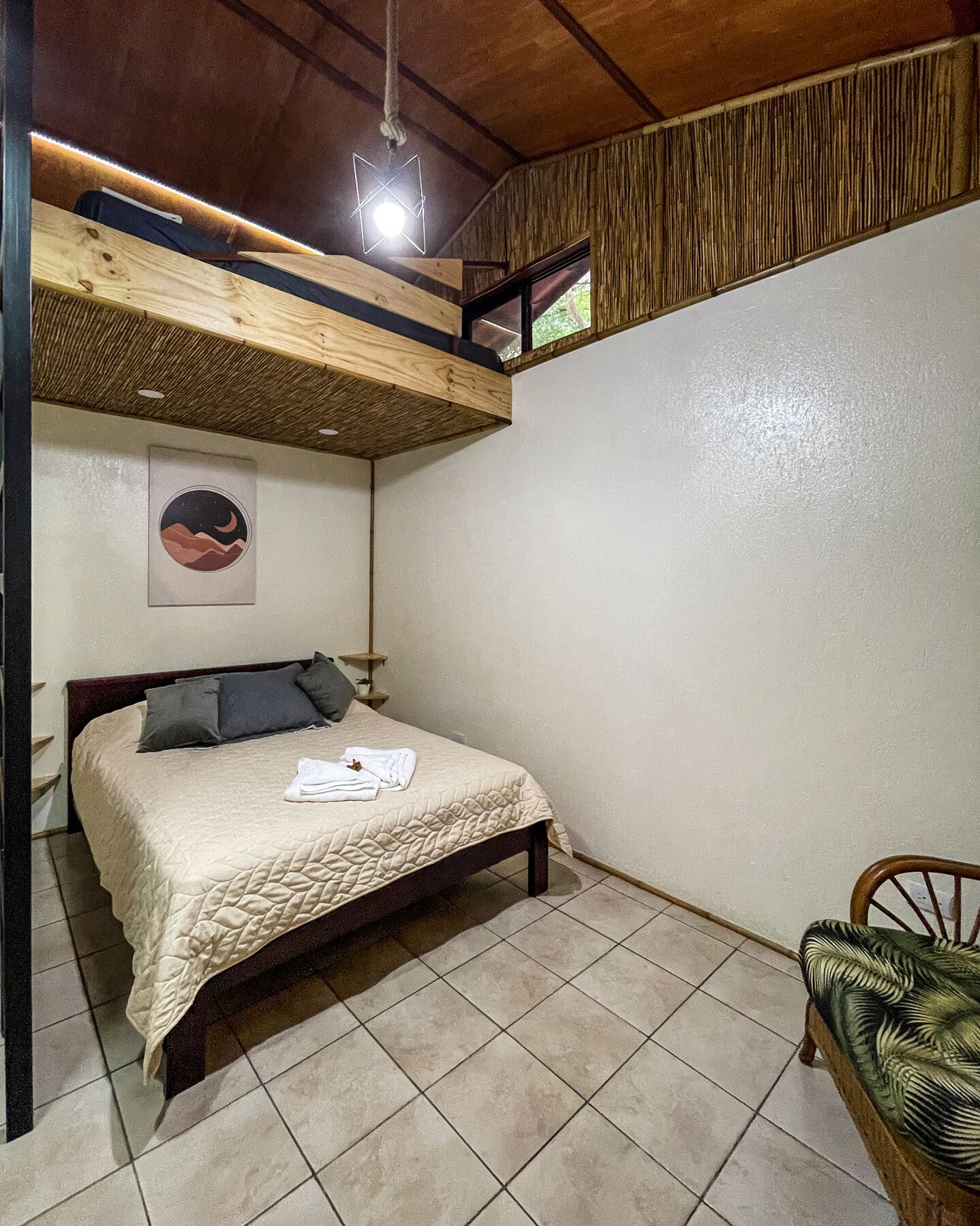 Un dormitorio con una litera, una cama con colcha, una silla y un cuadro circular en la pared.