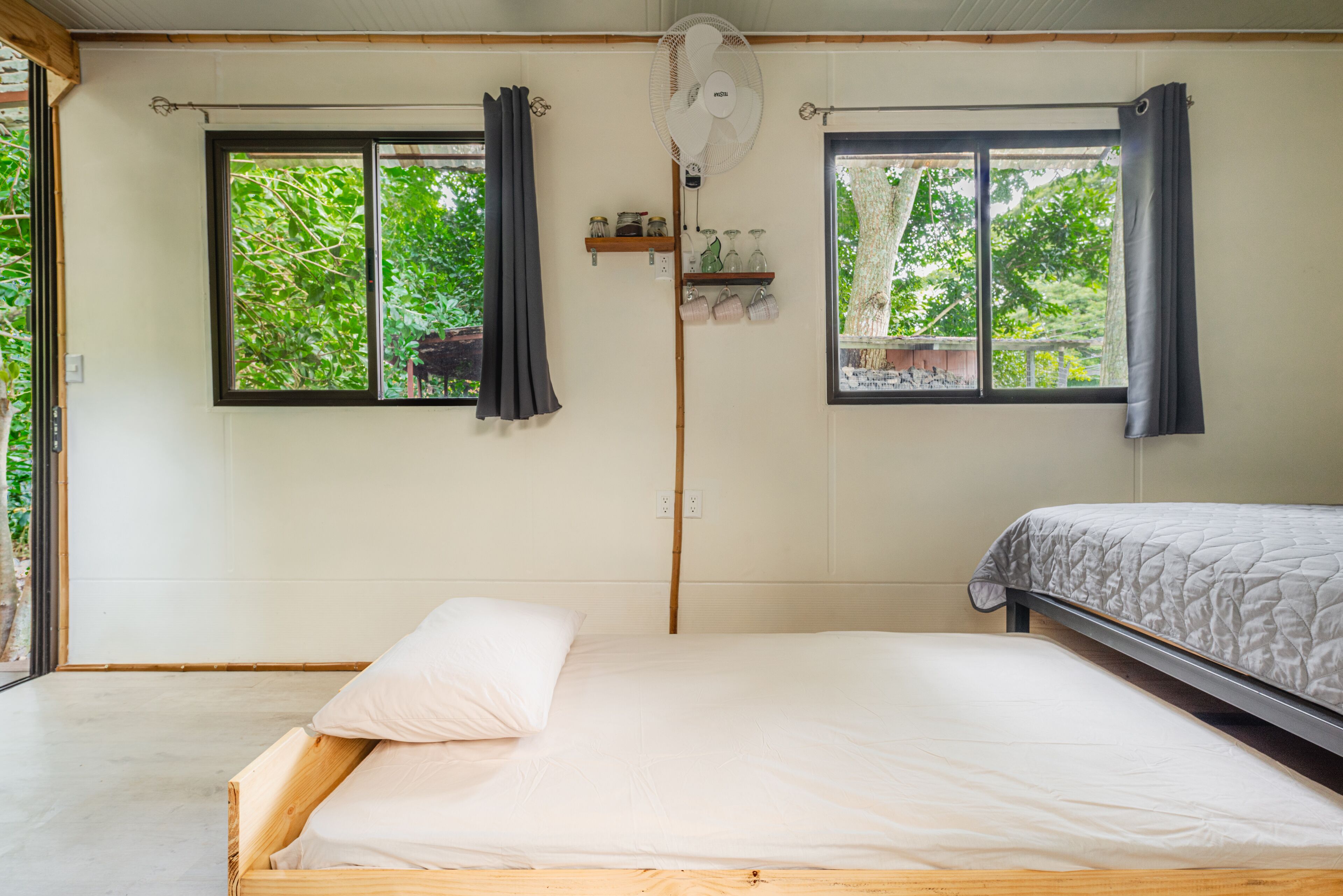 Una cama individual con estructura de madera, una mesita de noche y una ventana con vistas al verdor.