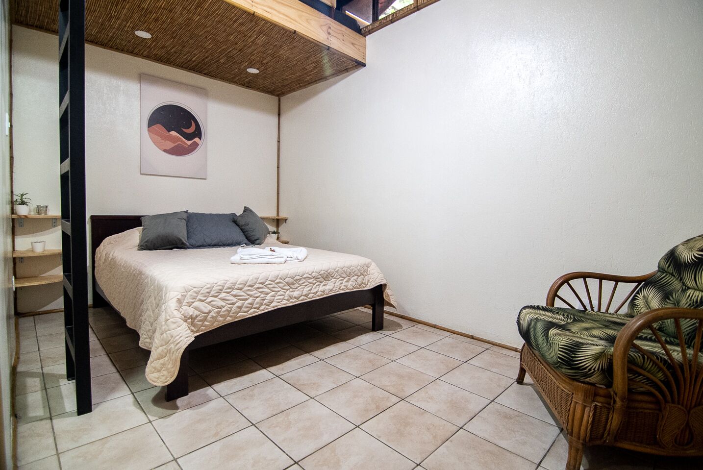 Una camera da letto con un letto, una sedia, uno scaffale con vari oggetti e un quadro appeso al muro.