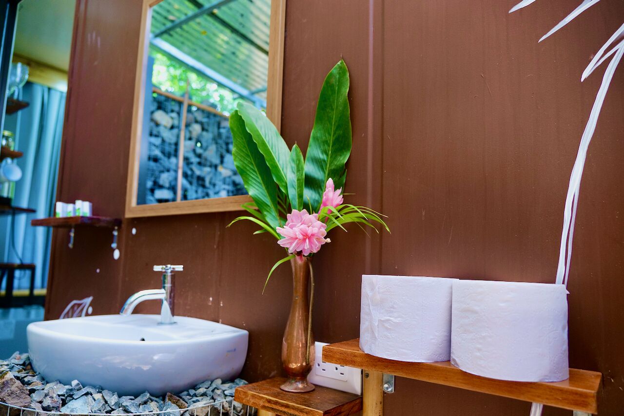A bathroom with a white sink, a vase with pink flowers, and a shelf with white towels.