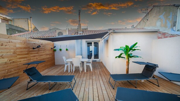 A rooftop patio with wooden flooring, a table and chairs, and several lounge chairs.