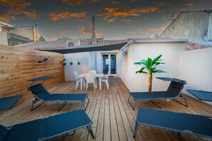 Een terras op het dak met houten vloer, een tafel met stoelen en meerdere lounge fauteuils.