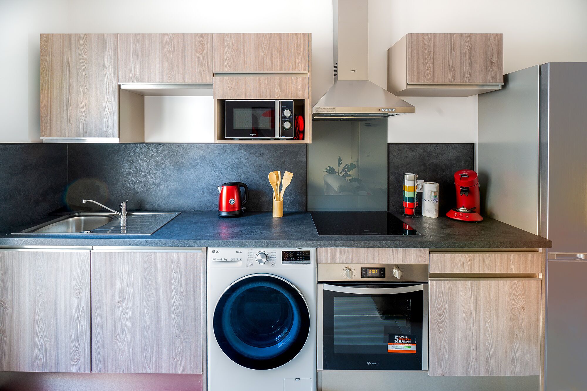 A modern kitchen with a washing machine, microwave, and coffee maker.