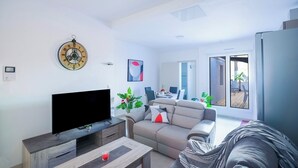 A modern living room with a flat-screen TV, a sofa, a coffee table, and a dining area in the background.