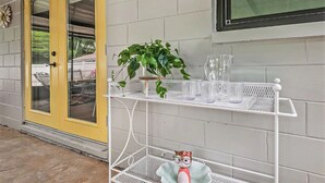 Eine gelbe Tür mit Glasfeldern, ein weißes Metallregal mit einer Topfpflanze und Gläsern sowie ein kleines Plüschtier auf einer unteren Ablagefläche.