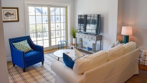 Een woonkamer met een blauwe fauteuil, een witte bank, een salontafel en een televisie.