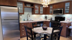 Cocina moderna con refrigerador de acero inoxidable, microondas y estufa. Hay una mesa de comedor con sillas y una araña colgante.