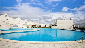 A large swimming pool with tiled deck, surrounded by white buildings with a modern architectural style.