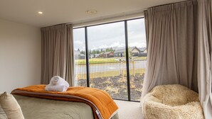 Ein Schlafzimmer mit großem Fenster, einem Bett, einem Sessel und Blick auf eine Wohngegend.
