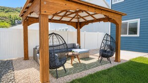 Une pergola en bois avec un toit en verre, deux fauteuils suspendus et une petite table.