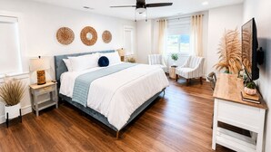 Une chambre à coucher moderne, comprenant un lit, des tables de chevet, un bureau, une chaise, un ventilateur de plafond et des œuvres d’art décoratives au mur.