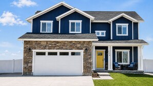 Une maison à deux étages avec une façade en pierre, un garage et un porche à l’avant, aménagé avec des sièges pour l’extérieur.