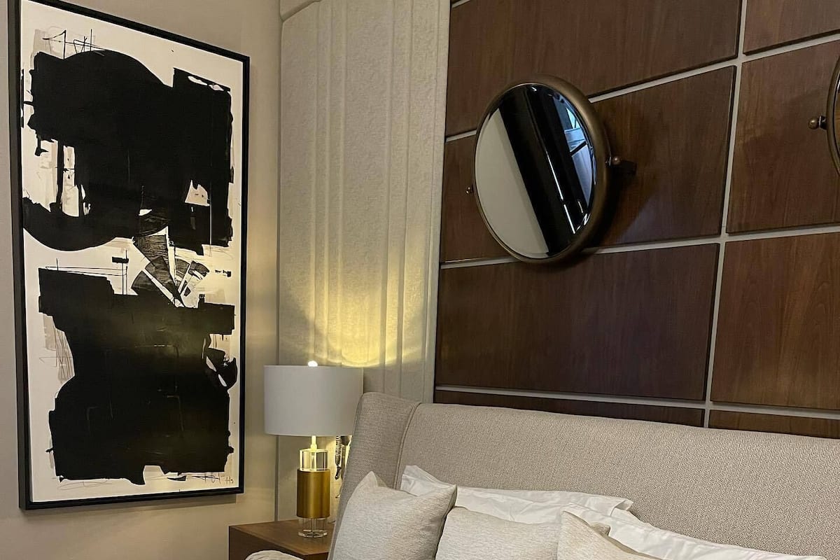 A neatly made bed with a textured blanket, a bedside table with a lamp, and a large abstract painting on the wall.