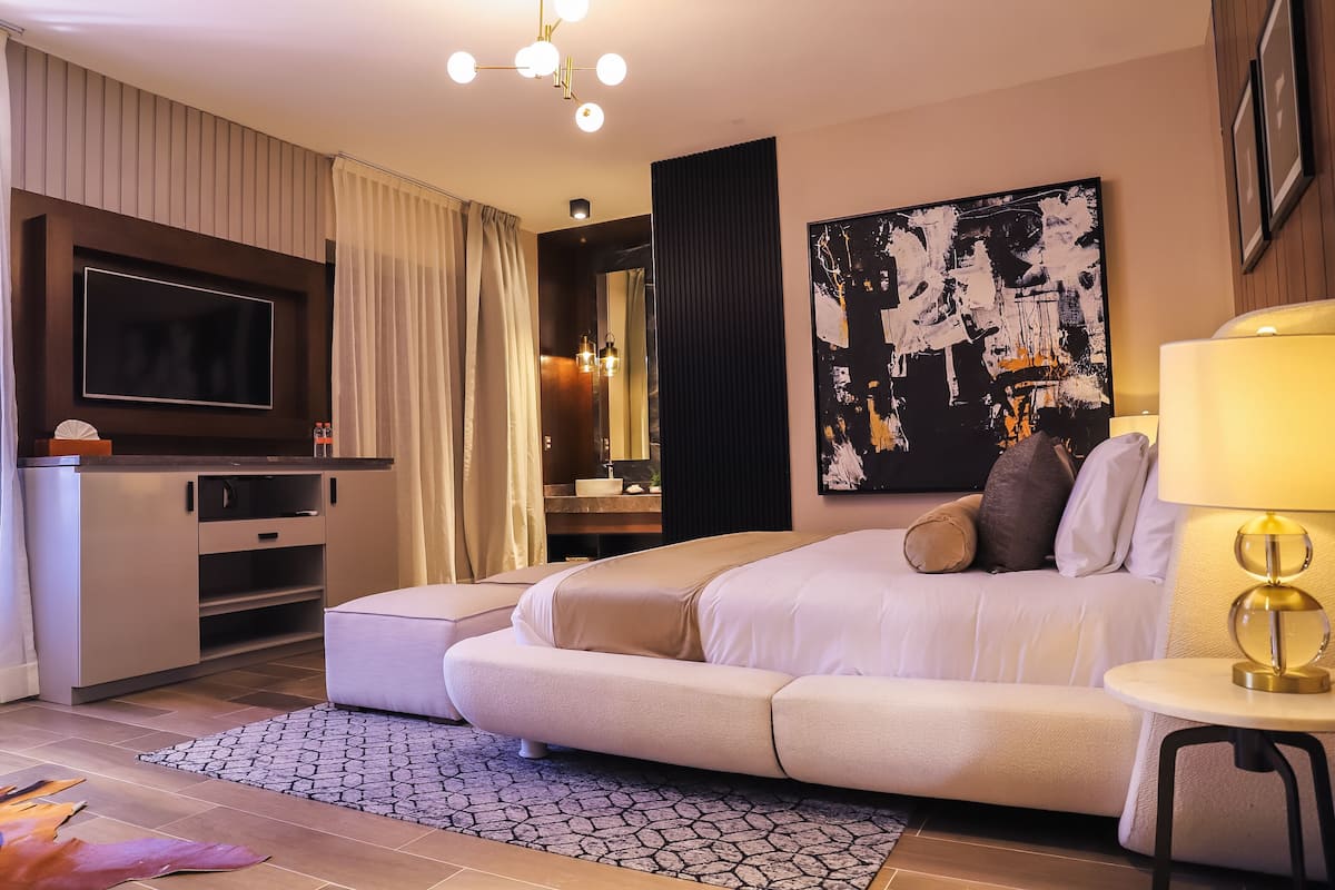 A modern hotel room with a large bed, a sofa, a TV, a desk, and a painting on the wall.