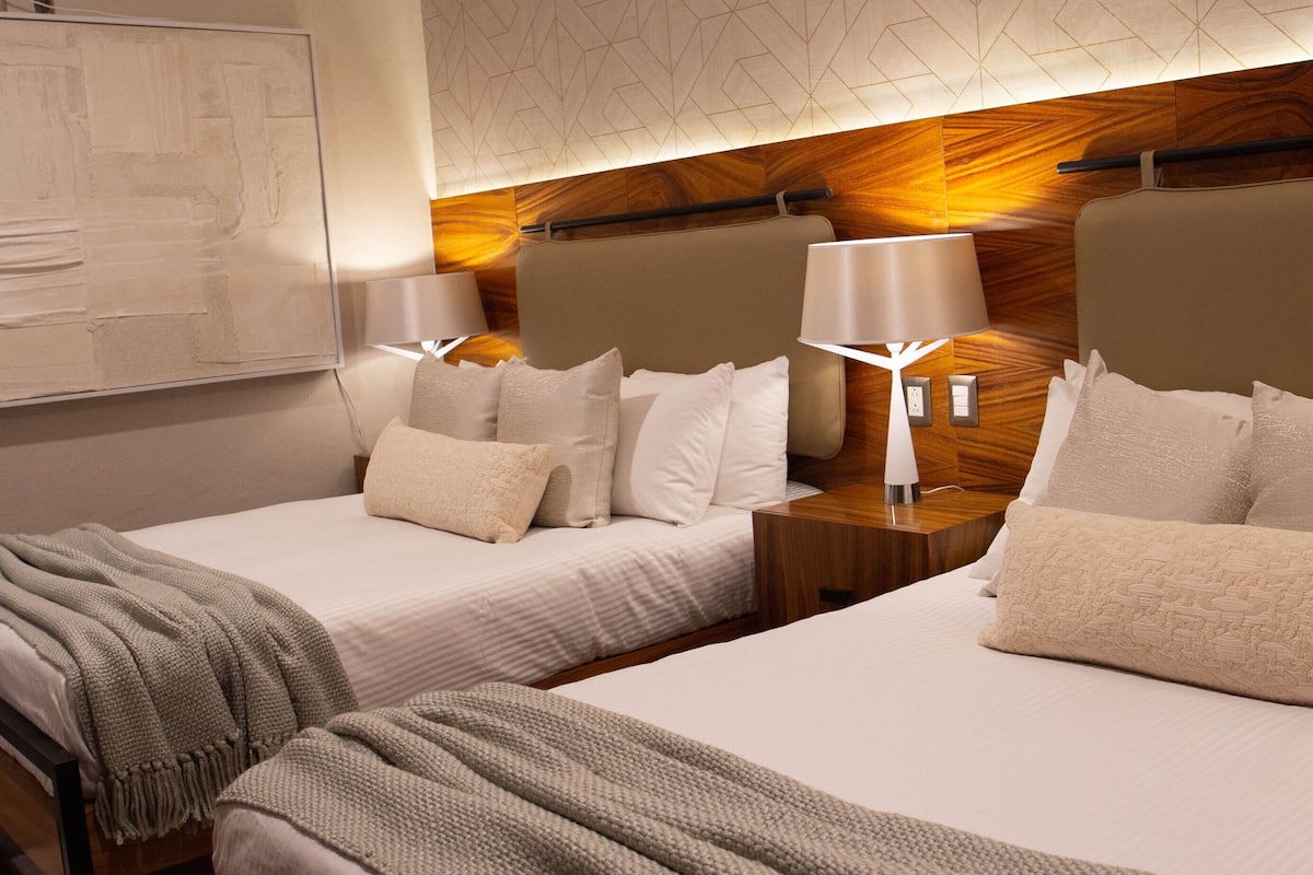A hotel room with two beds, a large artwork on the wall, and a geometric patterned ceiling.