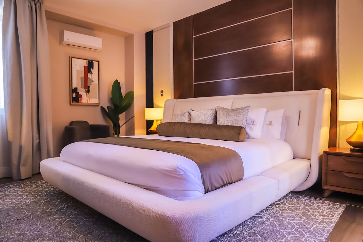 A modern hotel room with a large bed, a bedside table, a lamp, and a wall-mounted air conditioner.