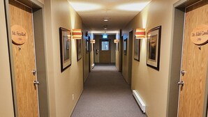 A hotel hallway with carpeted floors, wooden doors, and framed pictures on the walls.